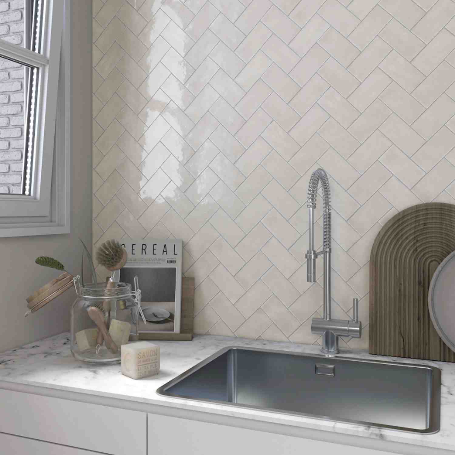 Terratinta Memorie Bianco Antico white glossy ceramic wall tiles in herringbone pattern kitchen backsplash with chrome faucet, window, and woven basket