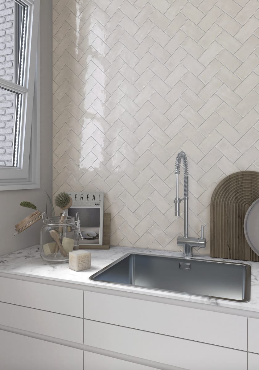 Terratinta Memorie Bianco Antico white glossy ceramic tiles in herringbone pattern kitchen backsplash with chrome pull-down faucet and window
