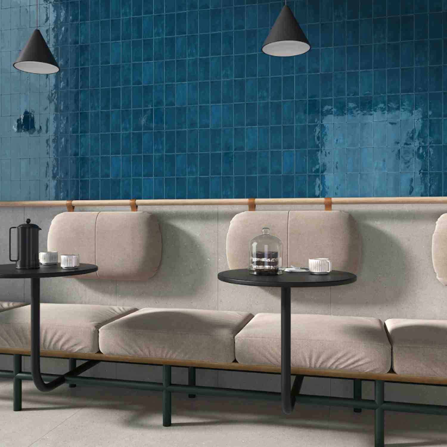 Terratinta Memorie Oltremare deep blue glossy ceramic wall tiles in café seating area with beige banquette, black cone pendant lights, and round side tables