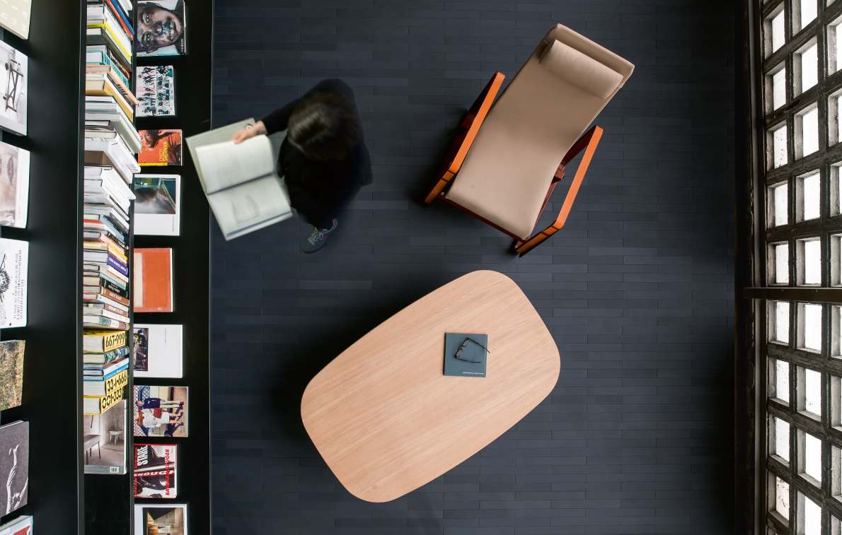 Mutina Mews Ink dark matte porcelain floor tiles in aerial view of reading room with leather lounge chair, wooden coffee table, bookshelf, and grid window