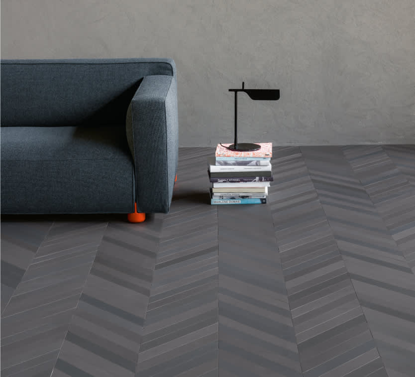 Mutina Mews Lead dark grey matte porcelain tiles in chevron floor pattern with teal sofa, stacked books, and black table lamp