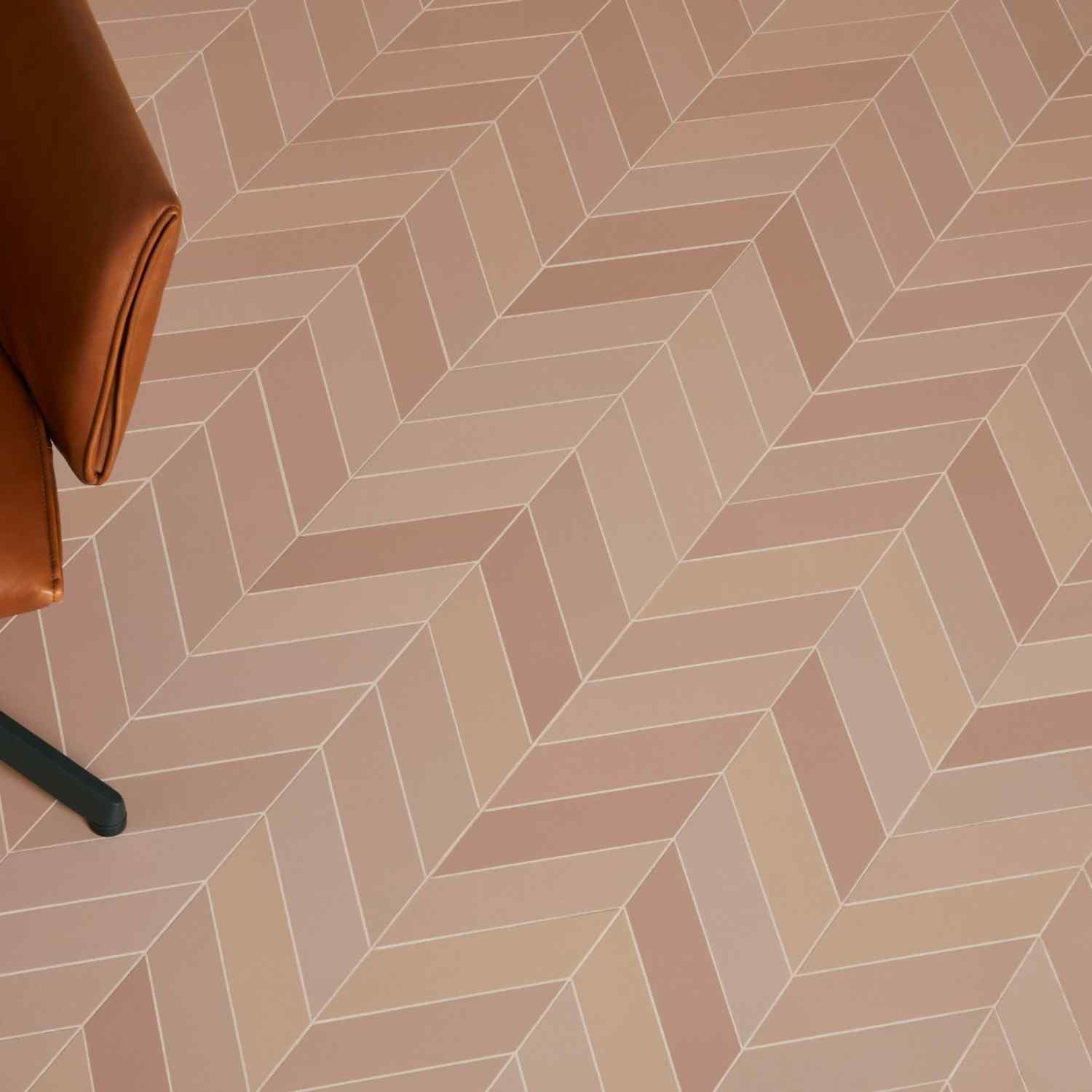 Mutina Mews Fog pink matte porcelain tiles in chevron pattern floor close-up with tan leather sofa edge