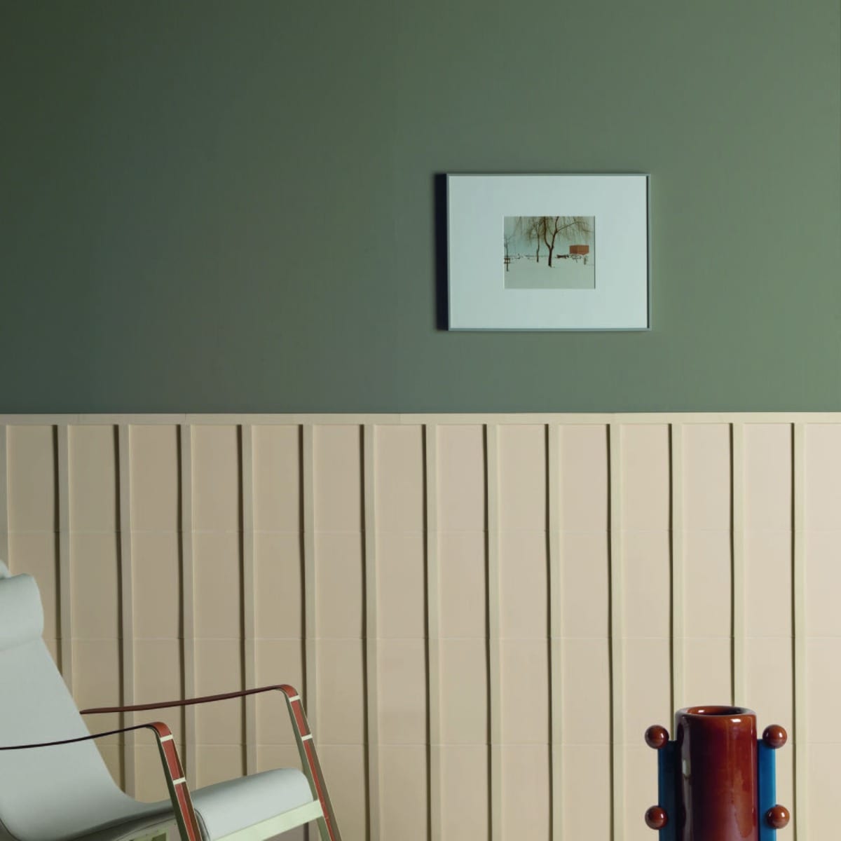 Motivo porcelain tile in cream installed as vertical wainscoting against a sage green wall in a styled living space with modern chair and decorative vase