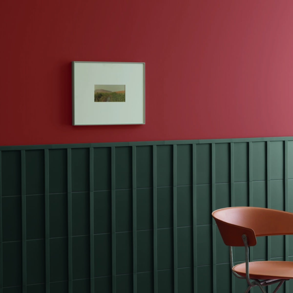 Motivo porcelain tile in dark green installed as vertical wainscoting against a burgundy wall in a contemporary room with framed artwork and terracotta chair
