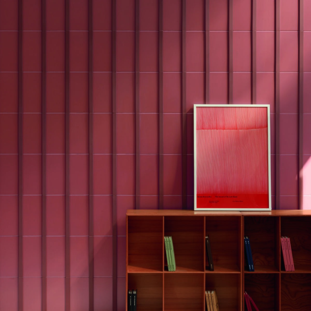 Motivo porcelain tile in deep rose installed as a full wall covering in a sunlit room with wooden bookshelf and framed red artwork