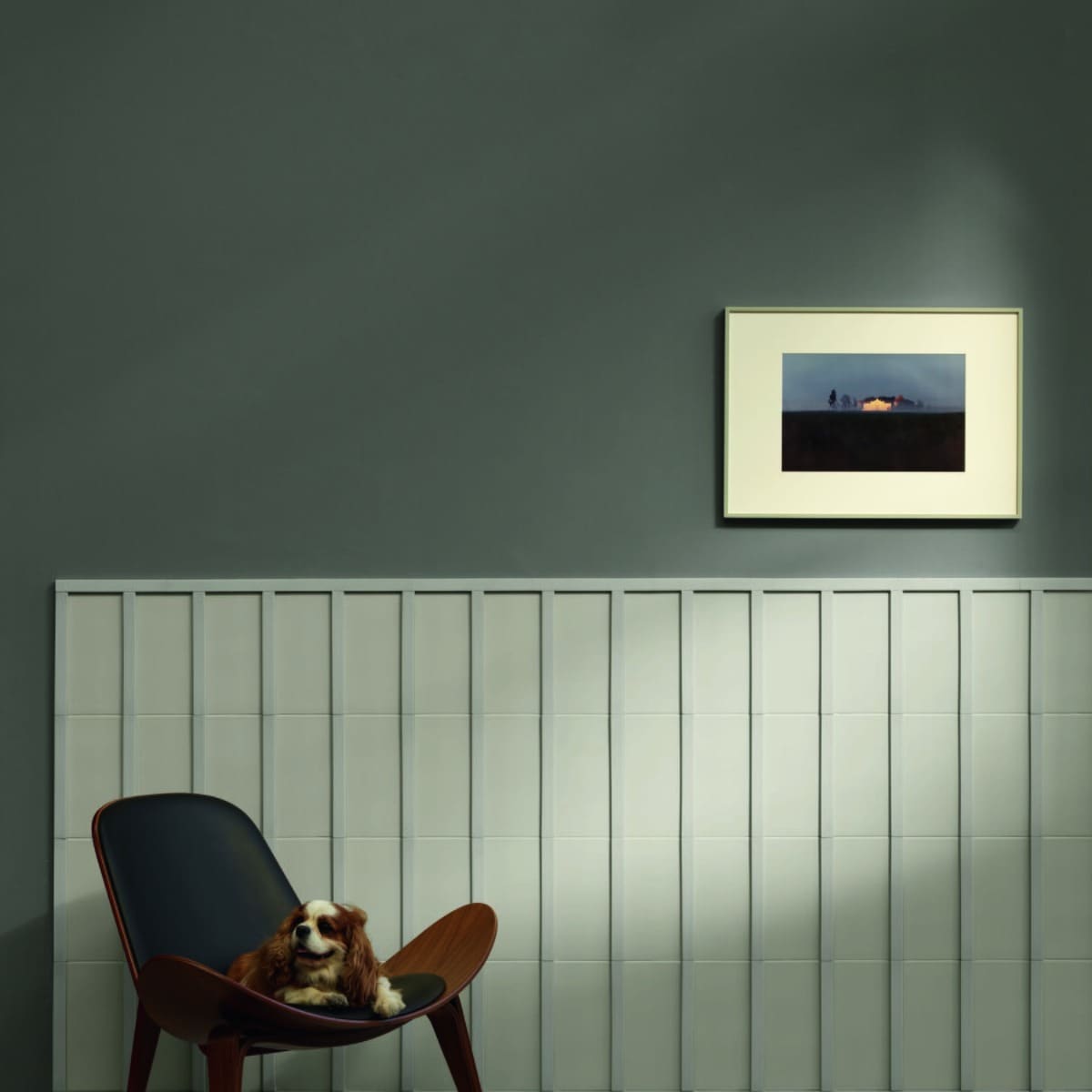 Motivo porcelain tile in light sage green installed as vertical wainscoting against a dark green wall in a styled room with mid-century shell chair and framed artwork