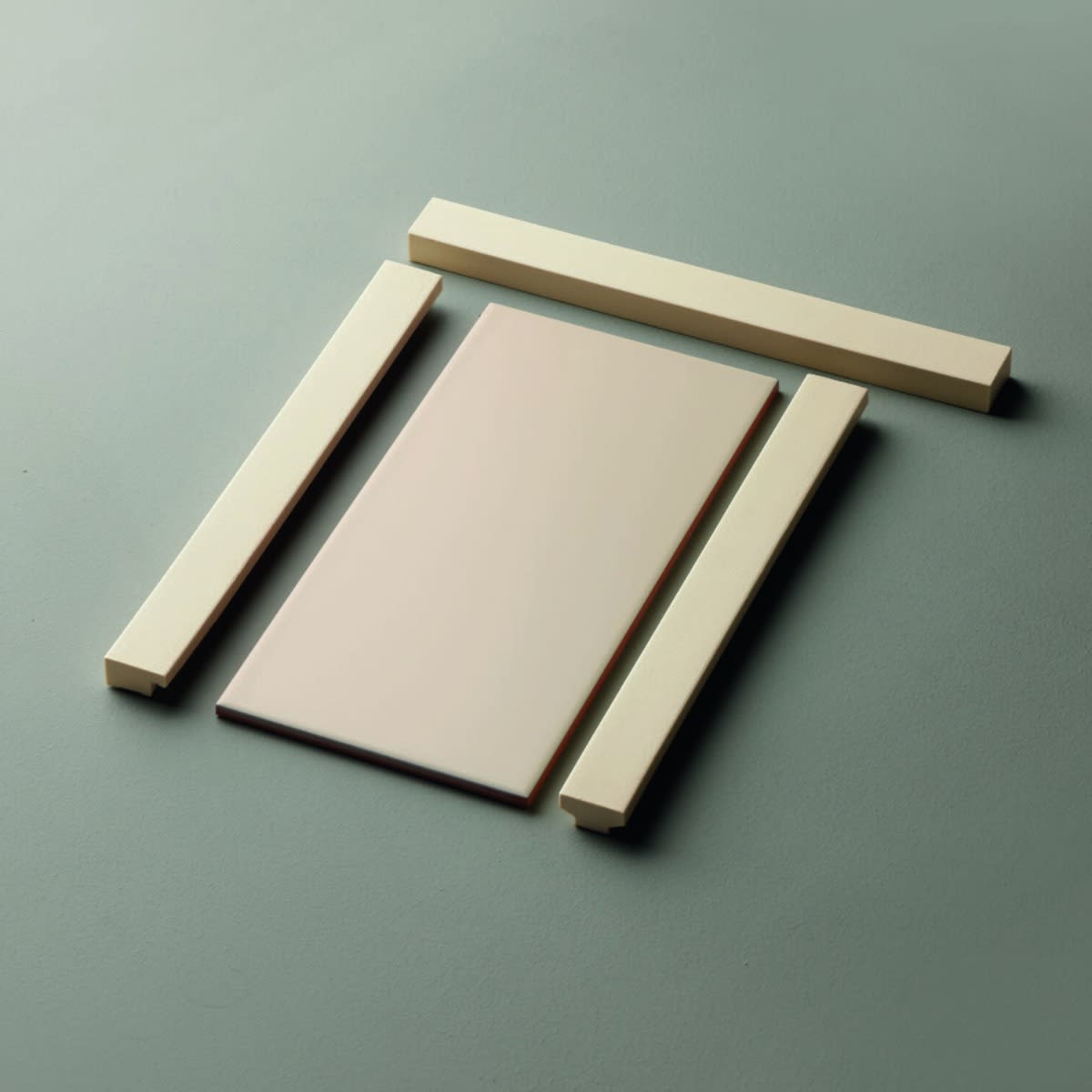 Motivo porcelain tile product detail showing blush pink field tile with cream-colored T-shaped and L-shaped trim pieces on a gray surface