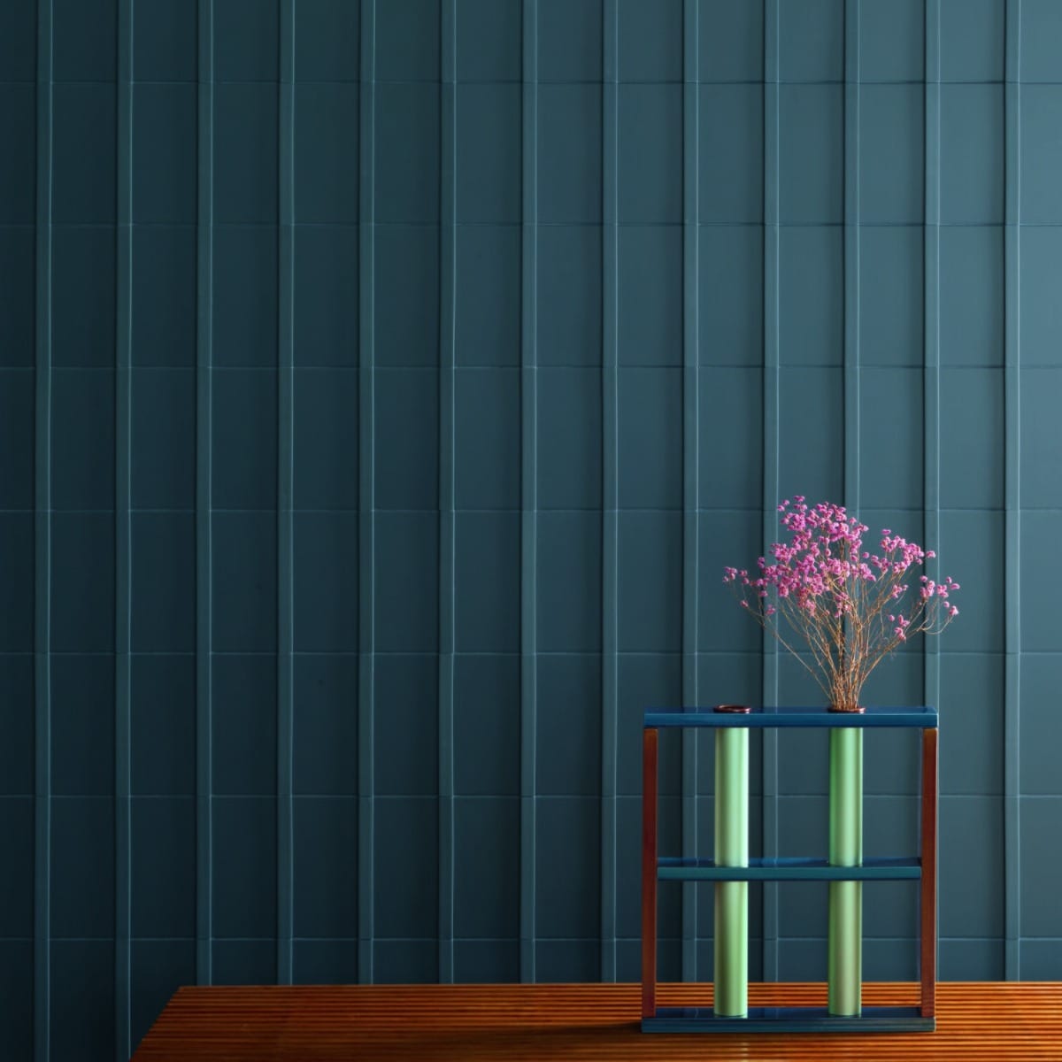 Motivo porcelain tile in dark teal installed as a full wall covering in a contemporary styled room with modern side table and pink flowers