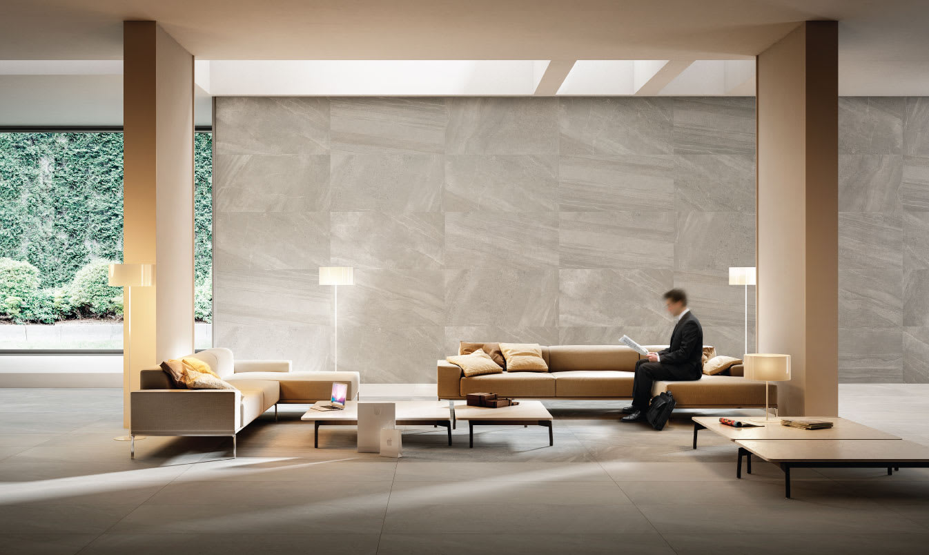 Impronta Nordic Stone Norvegia mosaic porcelain wall tiles in grey tones installed in a hotel lobby with garden view window, camel leather sofas, floor lamps, and modern minimalist furnishings