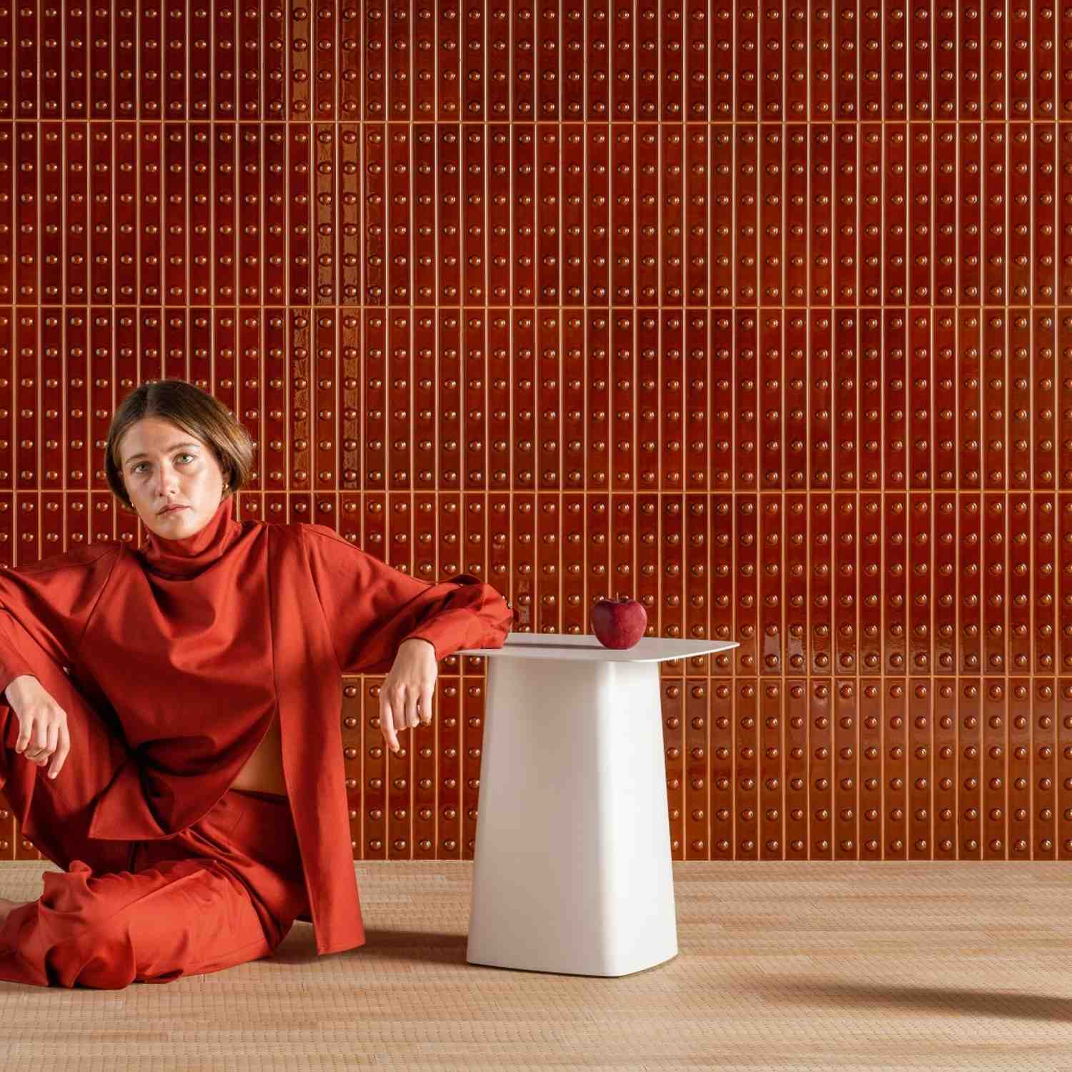 Mutina Punto glazed ceramic wall tiles in Red matte finish with raised dot texture covering full wall, editorial lifestyle scene with white pedestal table and red apple