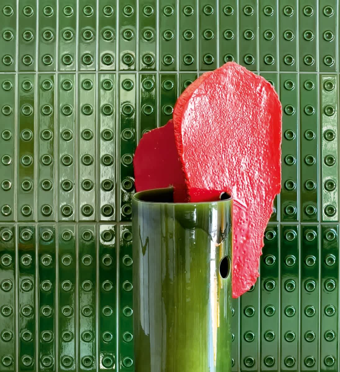 Mutina Punto glazed ceramic wall tiles in Vert green glossy finish with raised dot pattern, styled with bold red sculptural accent chair and green ceramic vase