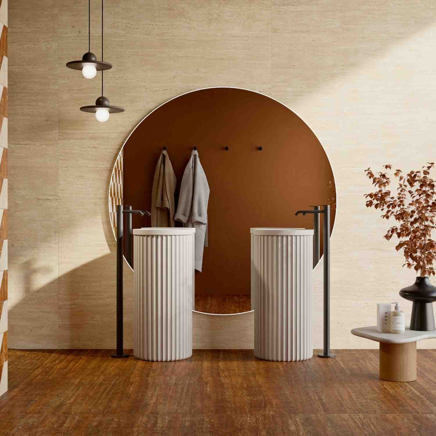 Ceramica Fioranese Senzatempo Trav porcelain stoneware tiles in Beige travertine-look on bathroom walls with large circular mirror, terracotta accent wall, twin white fluted pedestal sinks, black fixtures, pendant lights, and dried foliage in modern spa-i