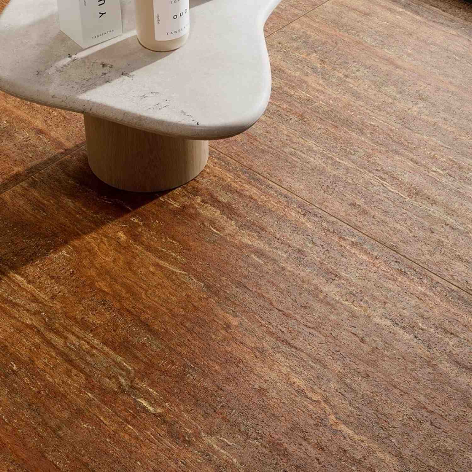 Ceramica Fioranese Senzatempo Trav porcelain stoneware floor tiles in Noce warm brown travertine-look close-up detail showing rich veining and natural stone texture with rounded wooden pedestal side table and bath products in bathroom setting
