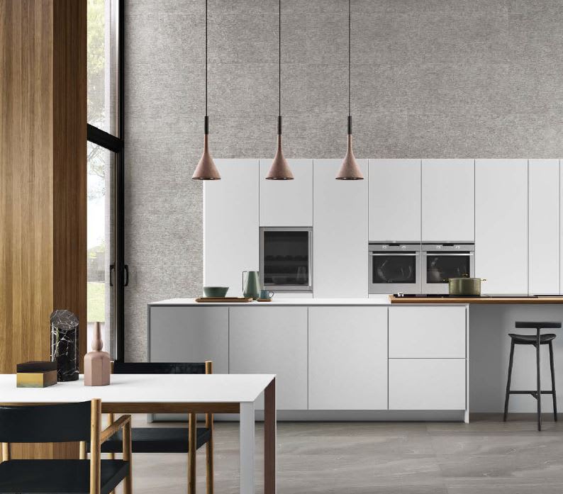 Ergon Stonetalk mosaic porcelain stoneware wall tiles in grey textured stone finish as kitchen backsplash in modern white kitchen with copper pendant lights, built-in ovens, wooden accents, dining table, and dark hardwood flooring