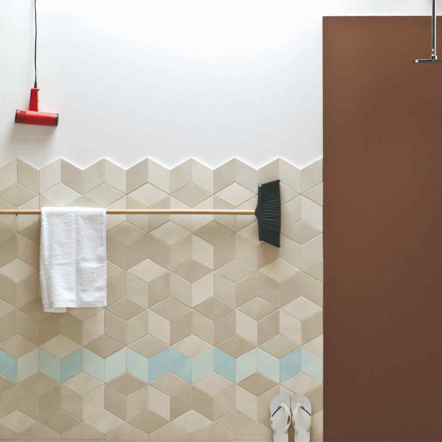 Mutina Tex ceramic wall tile bathroom with beige diamond-shaped three-dimensional textured tiles, white towel on brass rail, red wall lamp, and brown accent wall