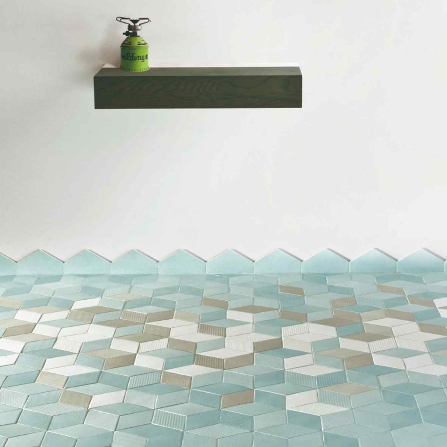 Mutina Tex ceramic wall tile display with multicolored three-dimensional chevron tiles in teal, blue, cream, and brown tones, floating dark shelf with vintage green lantern above