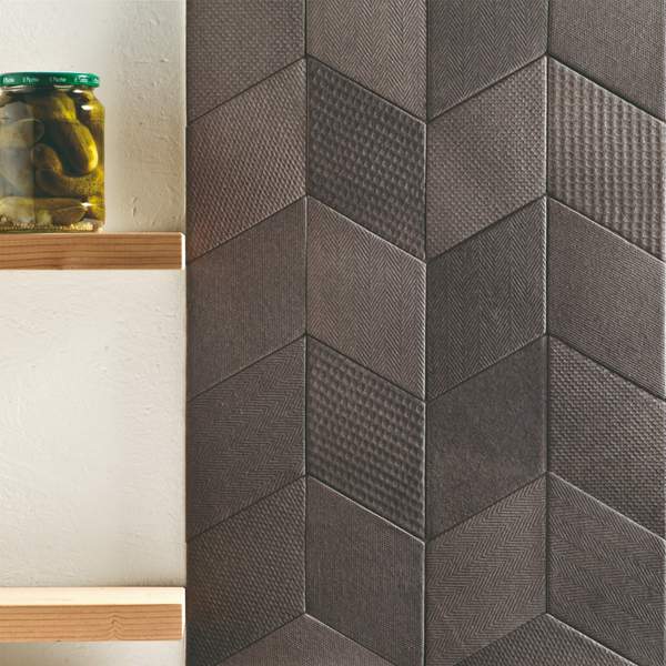 Mutina Tex ceramic wall tile thumbnail close-up of dark grey three-dimensional textured chevron tiles with wooden shelf and glass jar accent