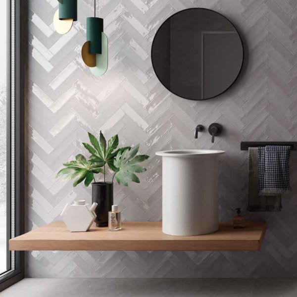 Ergon Total Brick ceramic wall tiles in grey herringbone pattern bathroom thumbnail with vessel sink, round mirror, and wooden floating shelf