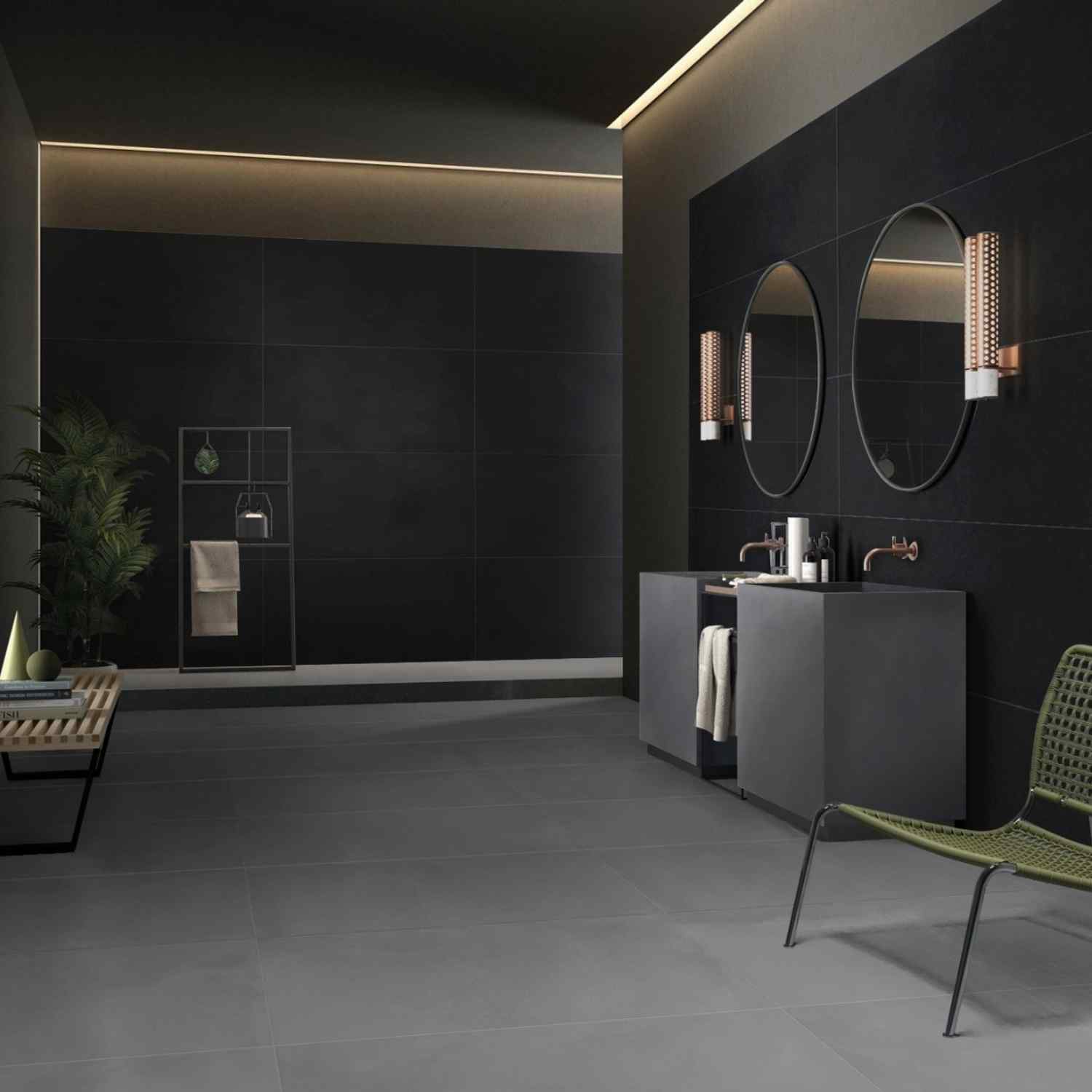Florina Urban Cement porcelain tiles in dark charcoal on walls and floor of a luxurious bathroom with oval mirrors, copper accent lighting, grey vanity, and green rattan chair
