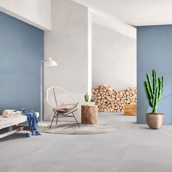 Florina Urban Cement porcelain floor tiles in light grey living room thumbnail with blue accent wall, wire chair, stacked firewood, and cactus plant