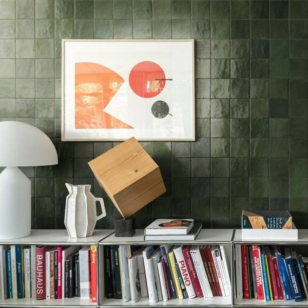 Marazzi Zellige glossy ceramic wall tiles in dark green with abstract art print, wooden sculpture, white lamp, and bookshelf display