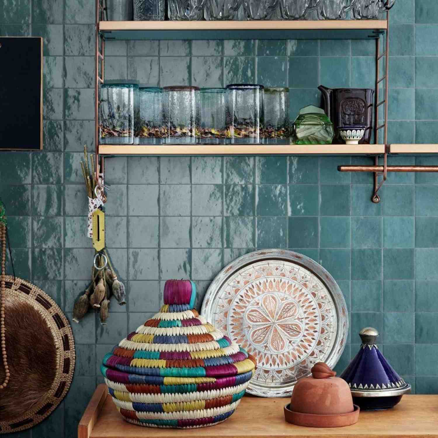 Marazzi Zellige glossy ceramic wall tiles in teal turquoise in kitchen with open wooden shelving, glass jars, colorful woven baskets, decorative ceramic plates, and terracotta tagine
