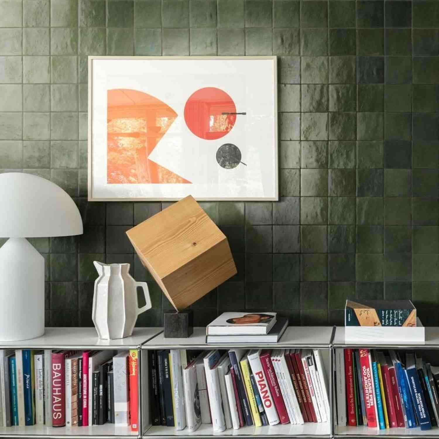 Marazzi Zellige glossy ceramic wall tiles in dark green with framed abstract art, bookshelf with colorful books, wooden sculpture, and white vase