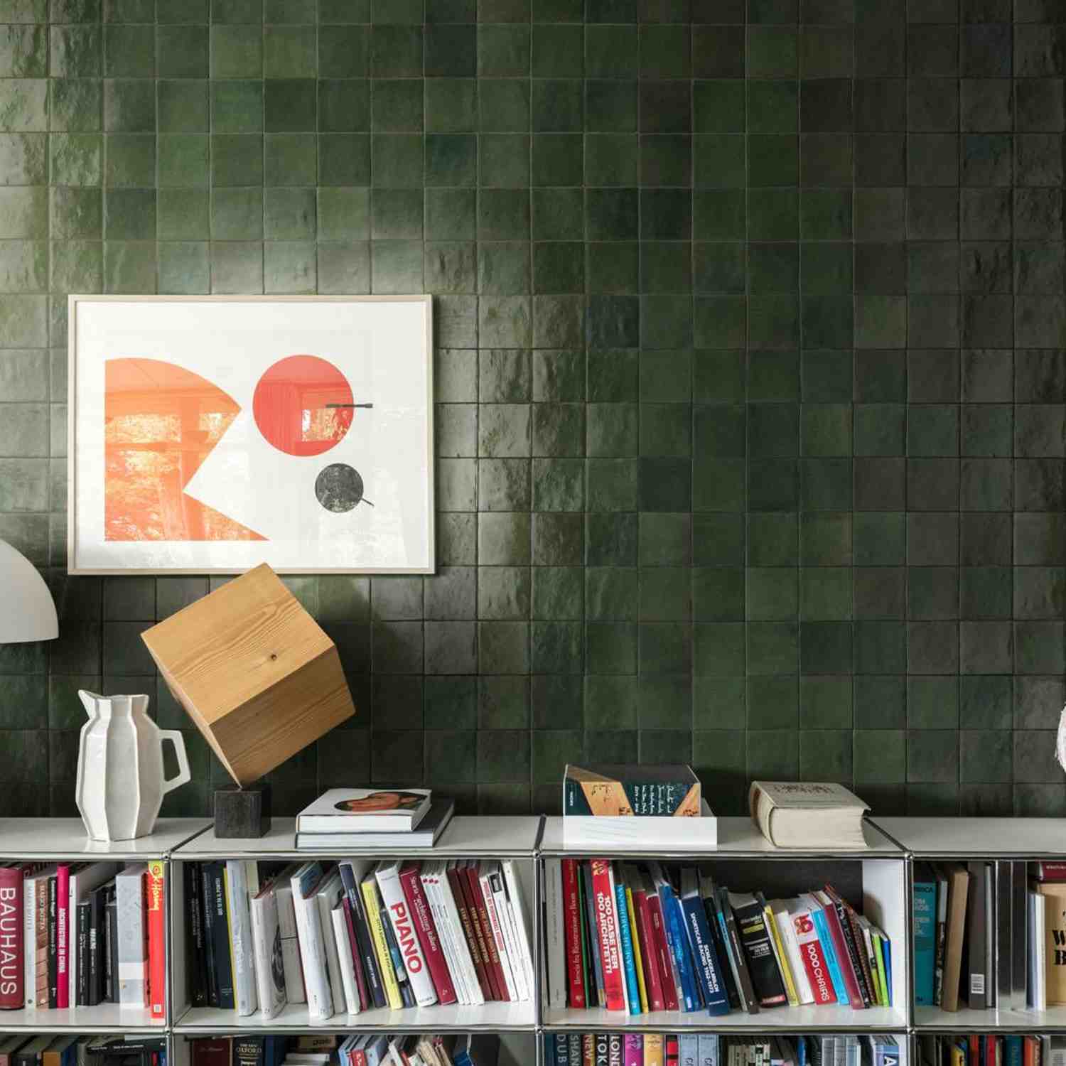Marazzi Zellige glossy ceramic wall tiles in dark green with framed abstract art, bookshelf, wooden geometric sculpture, and white vase